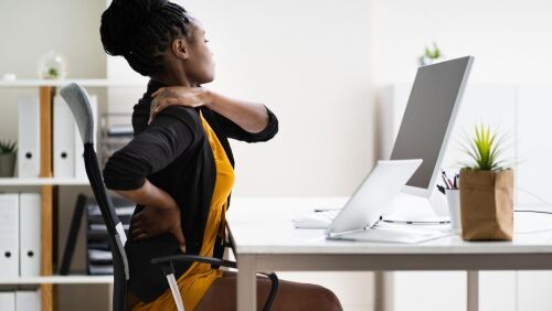 african american women at work in front of computer and grasping back neck in pain
